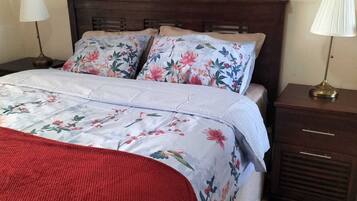 A neatly made bed with floral bedding, a red throw blanket, and two bedside lamps on wooden nightstands.
