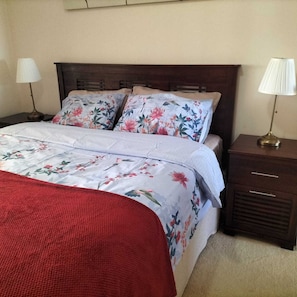 A neatly made bed with floral bedding, a red throw blanket, and two bedside lamps on wooden nightstands.