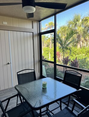 Ein Tisch mit Glasplatte, Stühle, Deckenventilator und Blick auf Grün.