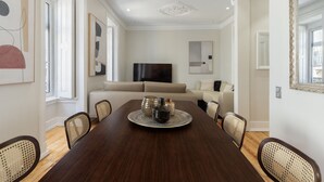 Un comedor con mesa de madera, sillas, televisor y sofá al fondo.
