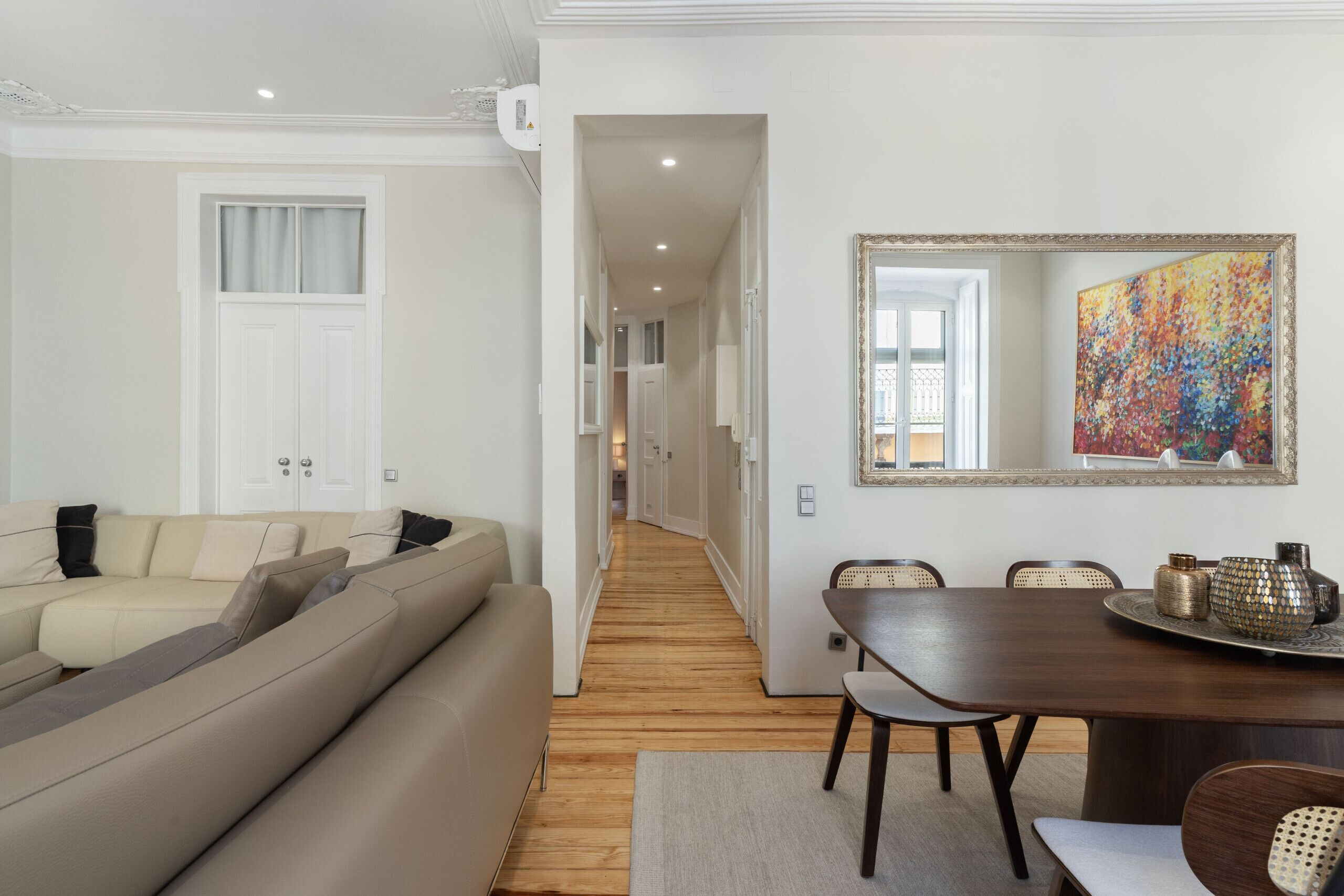 A modern living room with a sofa, dining table, chairs, and a hallway leading to other rooms.