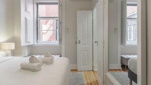 Una habitación de hotel con una cama, una mesita de noche con lámpara, una ventana y una puerta.