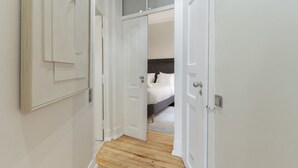 Un pasillo que conduce a un dormitorio con una cama, un armario y una puerta con un ventanal encima.