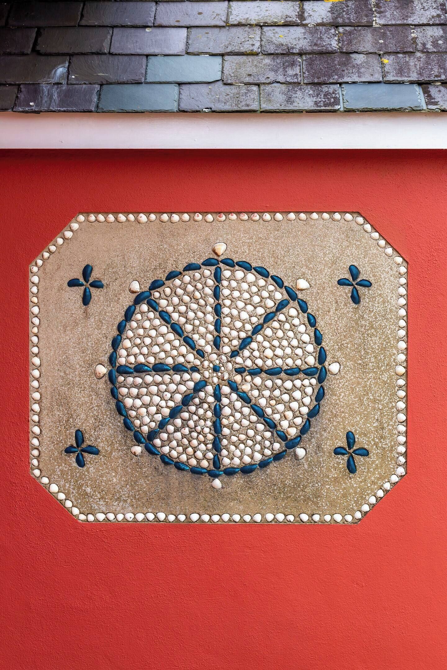 A decorative tile with a circular pattern and four flower designs on a red wall.
