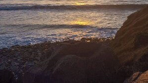 Ein Sonnenuntergang über dem Meer mit Wellen und Felsen im Vordergrund.