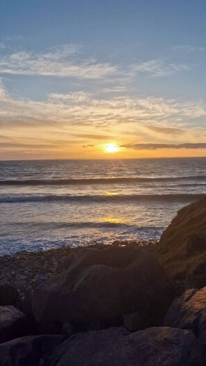 Ein Sonnenuntergang über dem Meer mit Wellen und Felsen im Vordergrund.