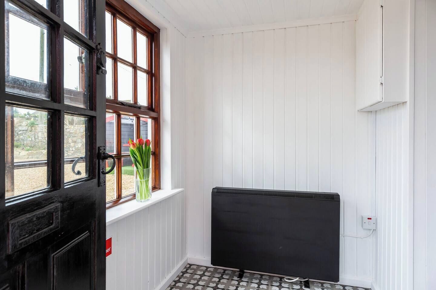 Ein Zimmer mit einer schwarzen Tür, einem Fenster mit Ausblick, einem Heizkörper und einer weißen Wand.