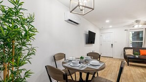 Een eetgedeelte met een ronde tafel voor vier personen, stoelen, een wandairconditioner en een televisie aan de muur.