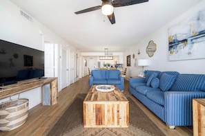 Ein modernes Wohnzimmer mit einem Holztisch, blau gestreiften Sofas und einem Essbereich im Hintergrund.