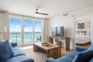 A room with a large sliding glass door leading to a balcony, a television on a wooden stand, a sofa, and a bed with a view. - Gulf front condo with resort amenities, steps to the beach (Destin)
