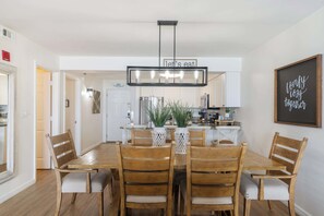 Ein Essbereich mit Holztisch und -stühlen, einer Chandelüster und einer Küche im Hintergrund.