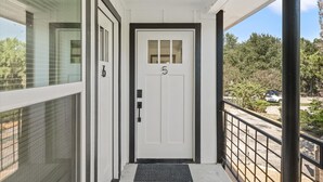 Une porte blanche portant le numéro 5, un paillasson noir et un balcon avec une rambarde en métal.