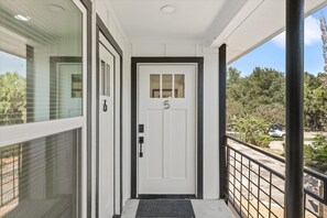 Eine weiße Tür mit der Nummer 5, eine schwarze Fußmatte und ein Balkon mit Metallgeländer.