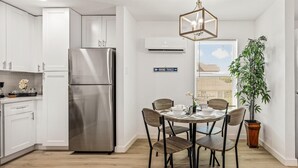 Une cuisine moderne avec des meubles blancs, un réfrigérateur en acier inoxydable et un coin repas comprenant une table ronde et des chaises.