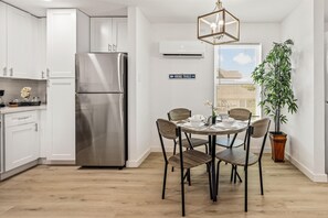 Eine moderne Küche mit weißen Schränken, einem Edelstahlkühlschrank und einem Essbereich mit rundem Tisch und Stühlen.