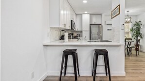 Une cuisine moderne avec des meubles blancs, un îlot central doté de tabourets, des appareils en acier inoxydable et un luminaire suspendu.