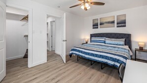 Un dormitorio con cama, ventilador de techo, mesita de noche y una pared decorada con tres cuadros.