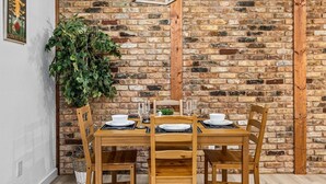 Un comedor con pared de ladrillo, mesa de madera y sillas.