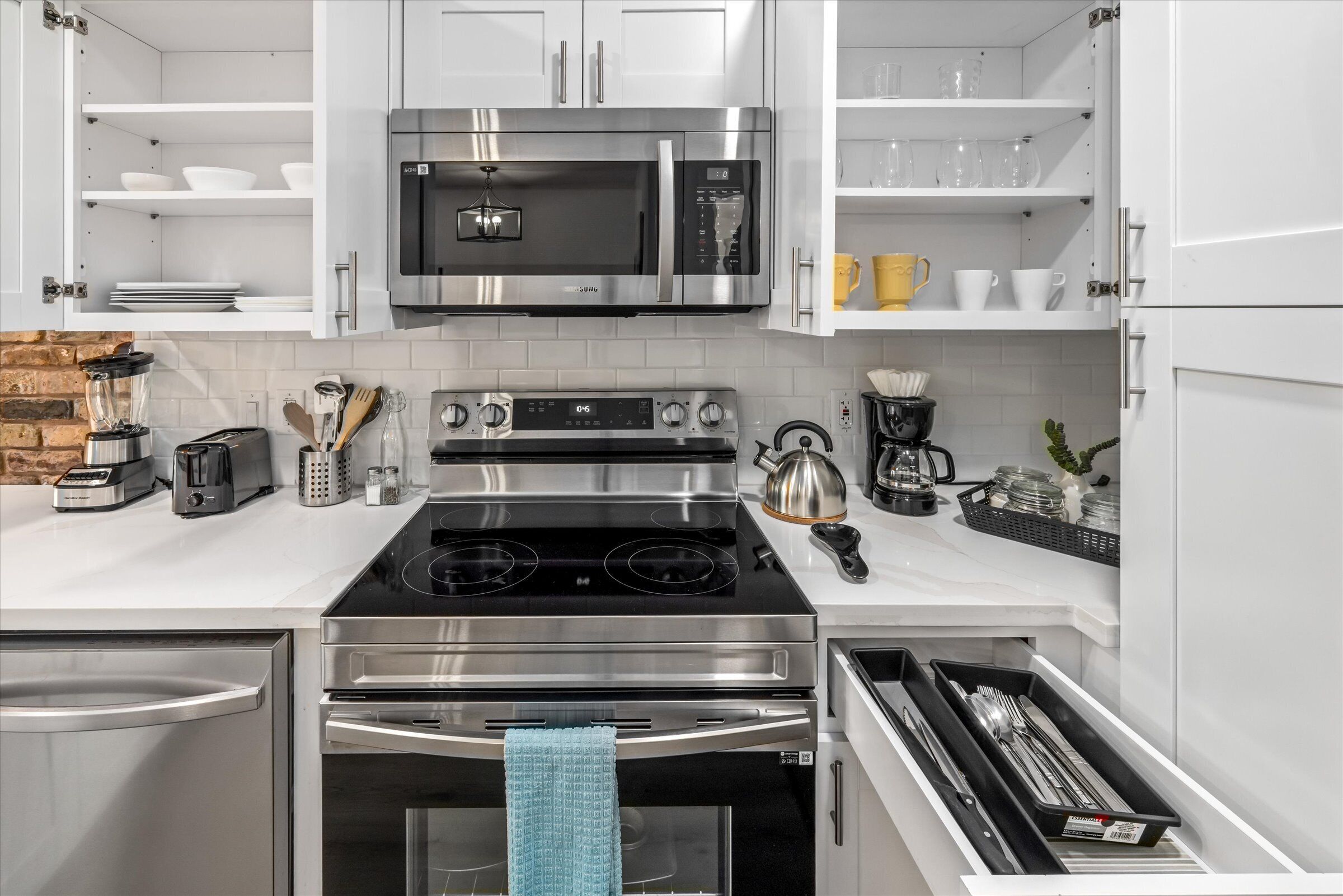 A modern kitchen with white cabinetry, a stainless steel stove, a microwave, and a coffee maker.