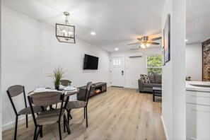 A modern living room with a dining area, a flat-screen TV, a ceiling fan, and a brick accent wall. - Pet-Friendly Montrose 1BR | Museum District | Free Parking<br>newly renovated (Houston)