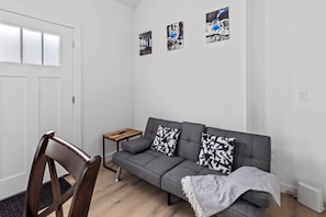 Een moderne woonkamer met een grijze bank, twee kussens met een patroon, een houten bijzettafeltje en een stoel.