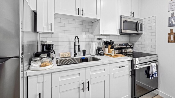 Een moderne keuken met witte kasten, roestvrijstalen apparatuur en een betegelde achterwand.