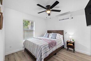 A bedroom with a bed, a ceiling fan, a bedside table with a lamp, and a window with blinds. - East Downtown - Pet-Friendly 1BR |Wi-Fi  | Free Parking<br>Newly Renovated (Houston)