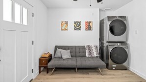 Een kamer met een grijze bank, een plafondventilator en gestapelde wasmachines.