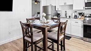 Een moderne keuken met witte kastjes, roestvrijstalen apparatuur en een eethoek met houten stoelen en een tafel voor vier personen.
