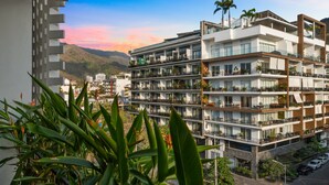 Un hotel de varios pisos con balcones, vista a la ciudad y una montaña al fondo.