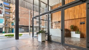 Una entrada de hotel moderna con suelo de piedra, grandes puertas de vidrio y paneles de madera.