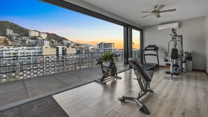 Un gimnasio moderno con equipo de ejercicio, ventilador de techo y un ventanal con vistas a la ciudad.