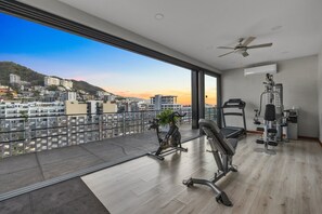 A modern gym with exercise equipment, a ceiling fan, and a large window with a city view. - Stylish studio close to beach restaurants and clubs (Puerto Vallarta)