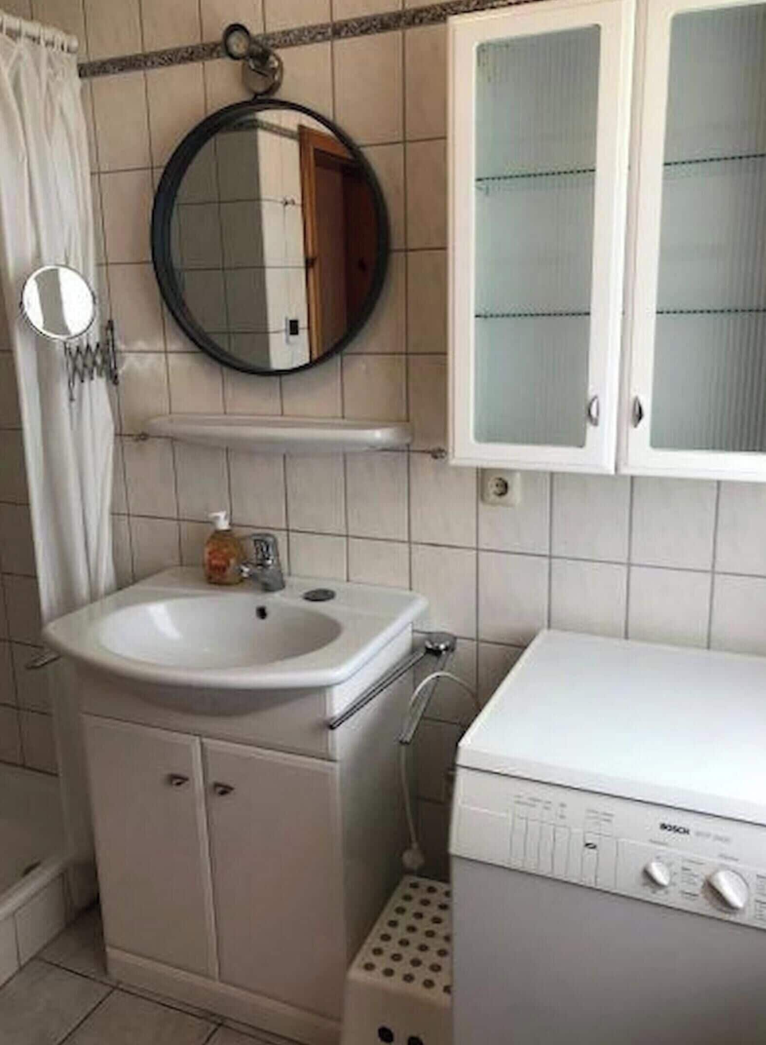 Ein Badezimmer mit Waschbecken, Spiegel, Schrank und einer Waschmaschine.