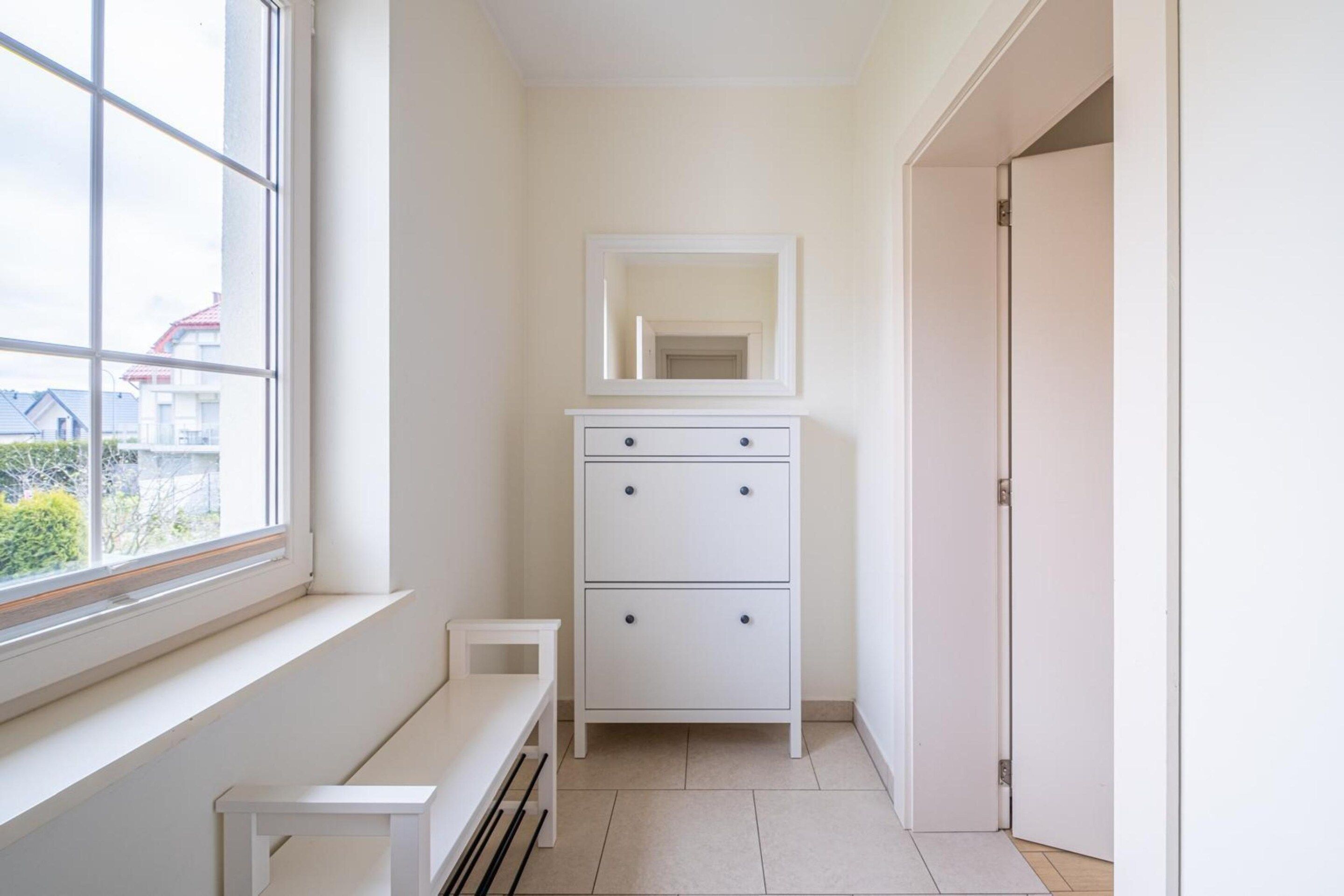 A narrow hallway with a white bench, a white dresser with a mirror, and a door.
