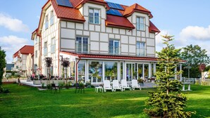 A large, multi-story building with a red-tiled roof, large windows, and a covered patio area with outdoor seating. - Comfortable Apartment for 4 People With a Balcony (Krokowa)