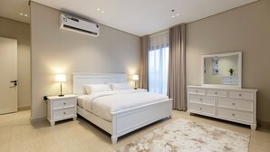 Een slaapkamer met een bed, nachtkastjes, een dressoir, een airconditioner en een raam met gordijnen.