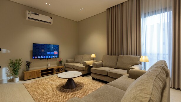 Een moderne woonkamer met een flatscreen televisie, twee banken, een salontafel en een groot raam met gordijnen.