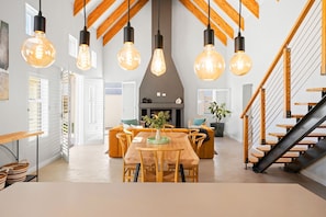 A modern interior with a wooden dining table, chairs, hanging light fixtures, and a staircase.