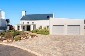 Uma casa moderna com calçada pavimentada, portões de garagem e um jardim bem cuidado.