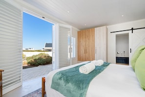 A bedroom with a bed, a wooden wardrobe, a bathroom with a shower, and a view of the outside.