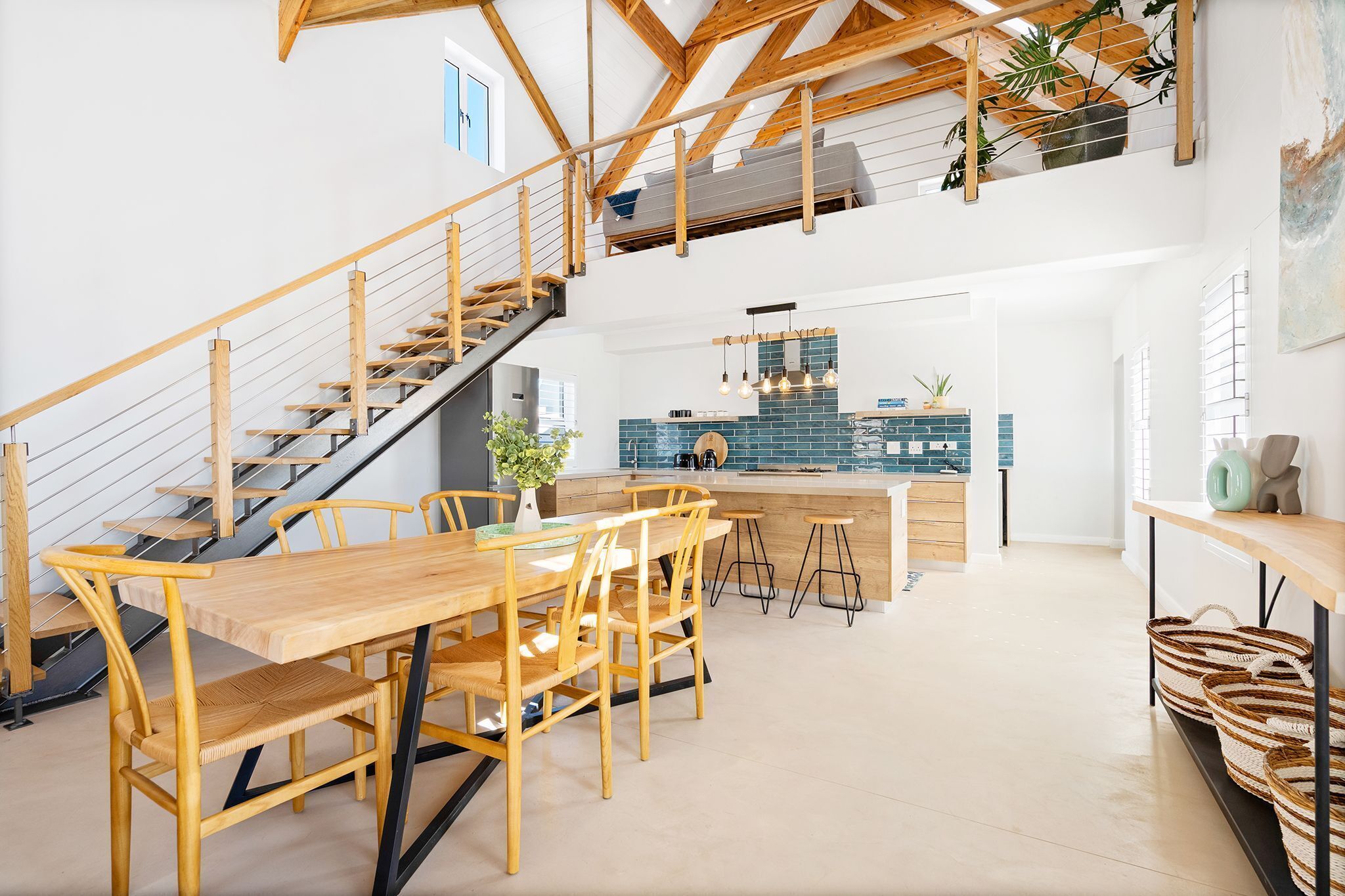 A spacious kitchen with a central island, wooden staircase, and a dining area with a long table and chairs.