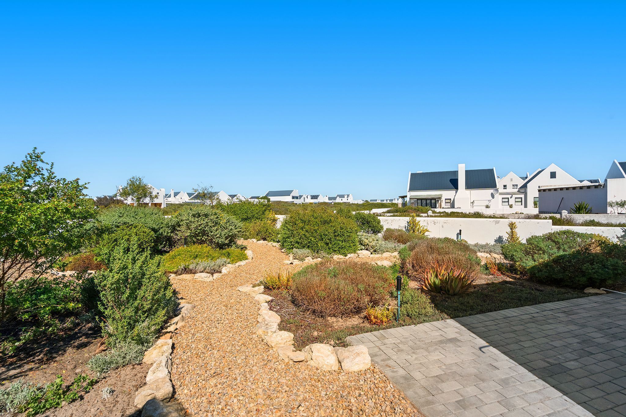 A residential area with modern houses, a paved walkway, and landscaped gardens.