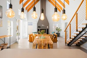 A modern interior with a wooden dining table, chairs, hanging light fixtures, and a staircase. - Waterbird Coastal Retreat (Bergrivier)