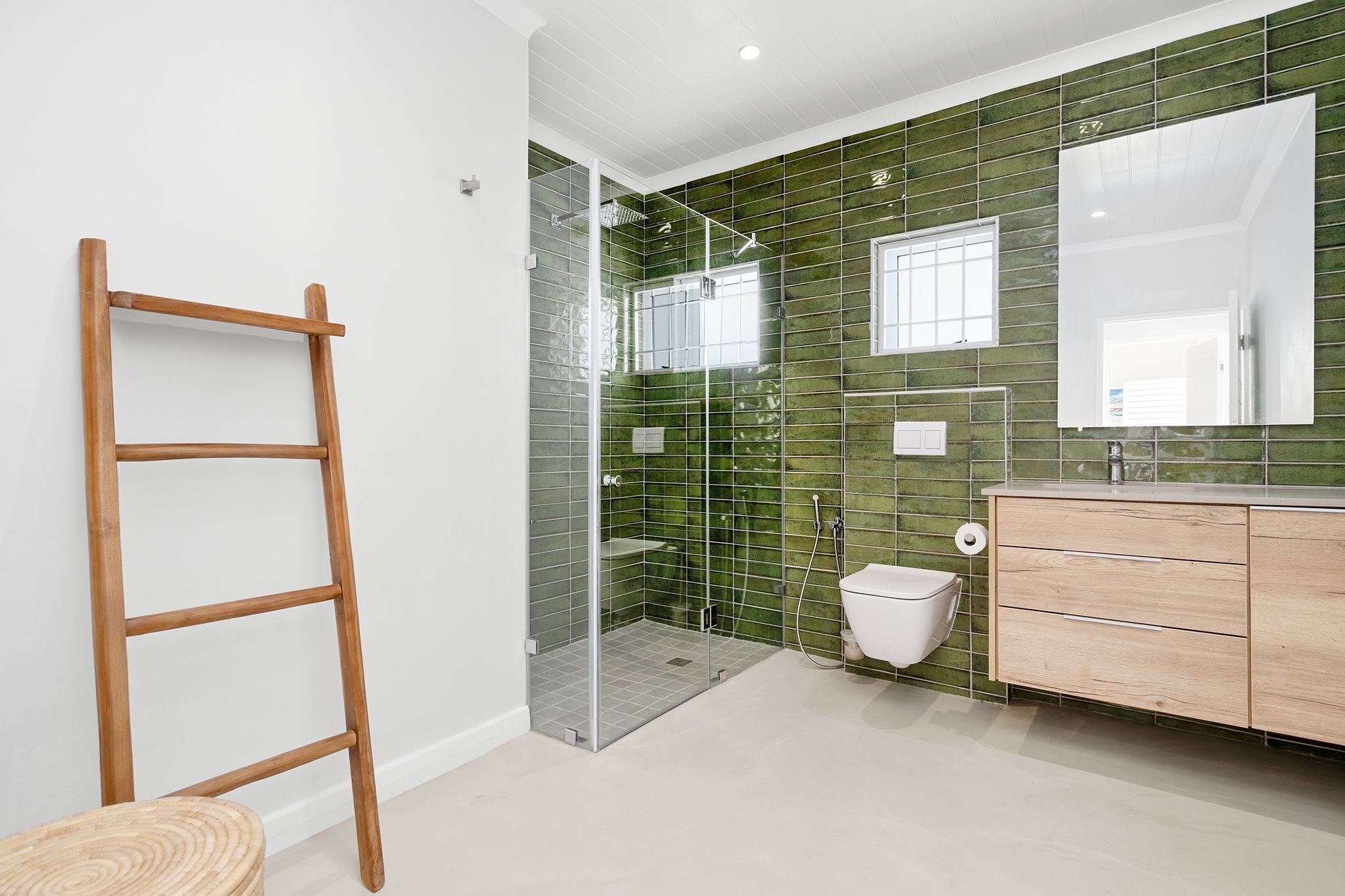 A bathroom with a glass-enclosed shower, a wooden ladder, a white toilet, and a vanity with drawers.
