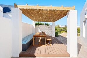 A wooden deck with a table and bench, a pergola overhead, and a white wall with a window. - Waterbird Coastal Retreat (Bergrivier)