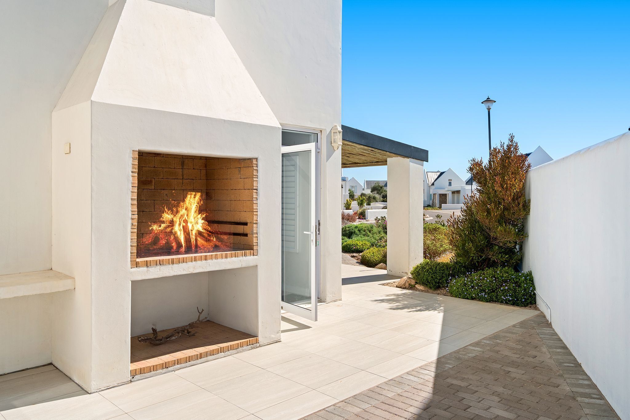 A modern outdoor fireplace with a brick surround, a clear glass door, and a paved patio area.