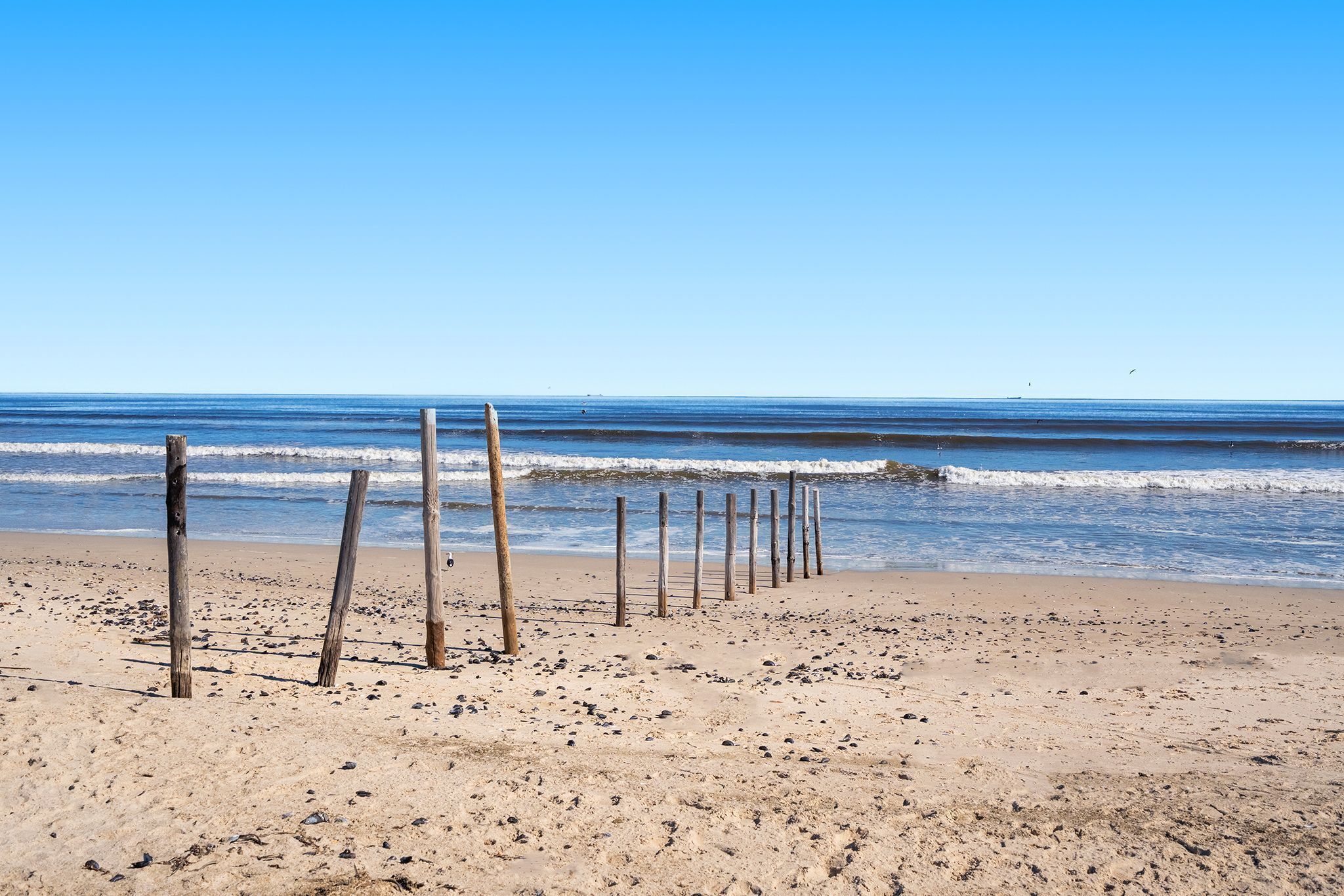 Een zandstrand met houten palen en golven op de achtergrond.