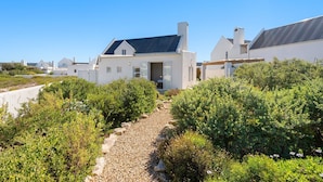 Una casa moderna con techo de paneles solares, rodeada de vegetación y un camino de grava.