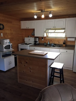 A compact kitchen with wooden cabinets, a microwave, a stove, a coffee maker, and a small island with stools.